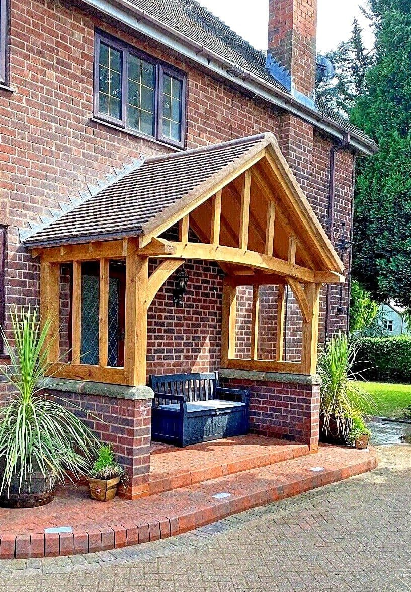 The Stroud oak porch on a red-brick home — grand curved beam over stone-capped dwarf walls, with a bench beneath the gable