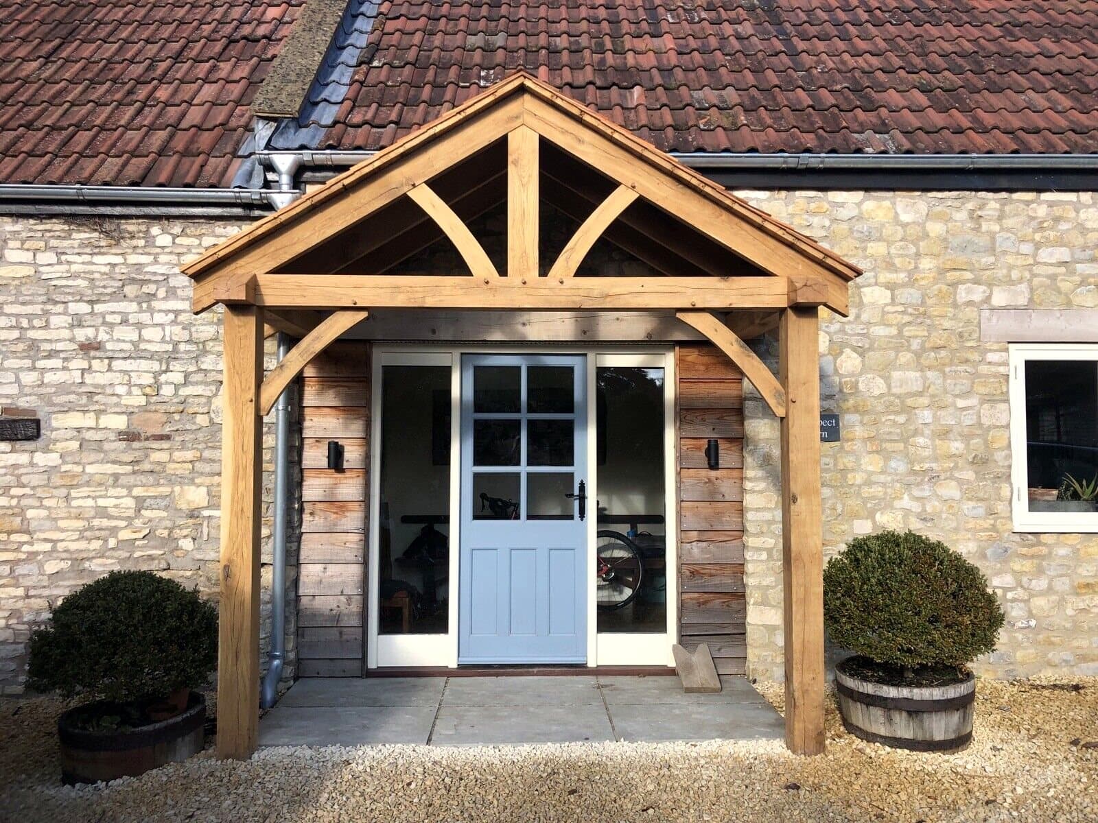 The Dursley oak porch on a stone barn conversion — full-height posts and splayed gable framing wide glazed doors