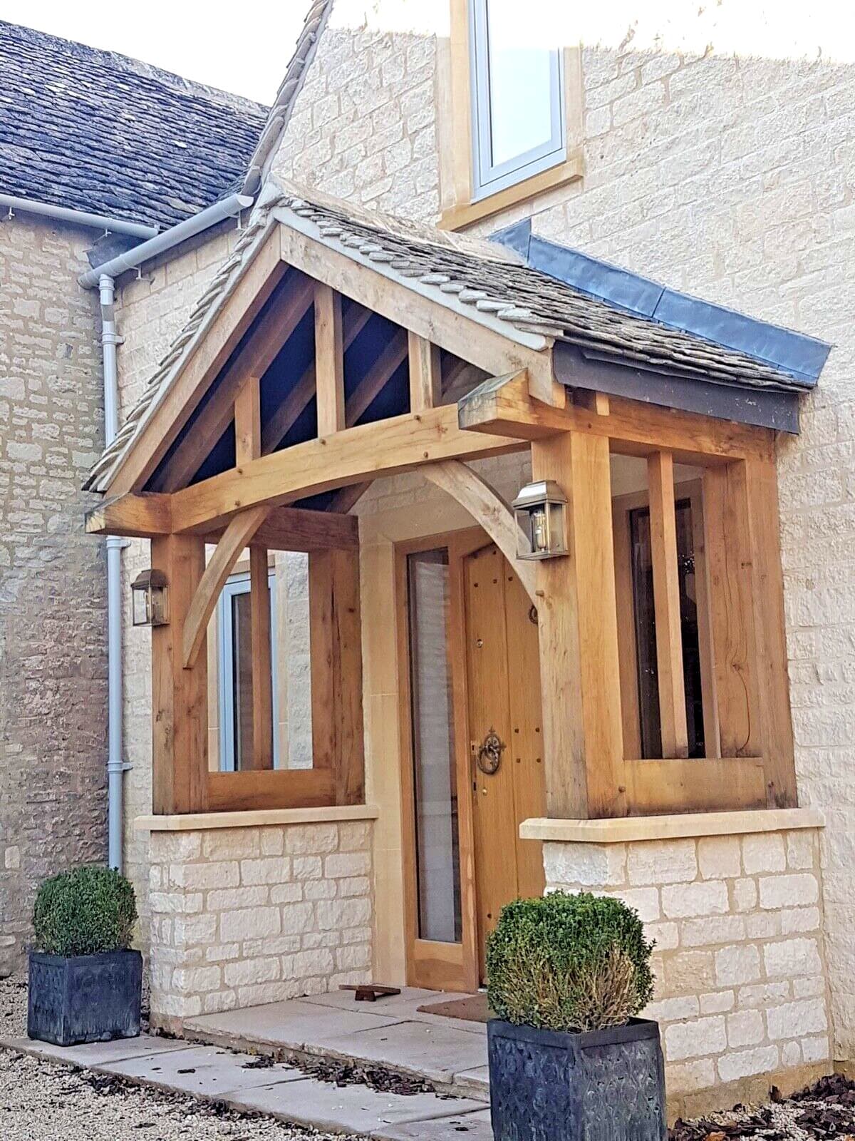 The Ludlow oak porch on a Cotswold stone house, with curved beam, side screens and a stone-tiled roof matching the property