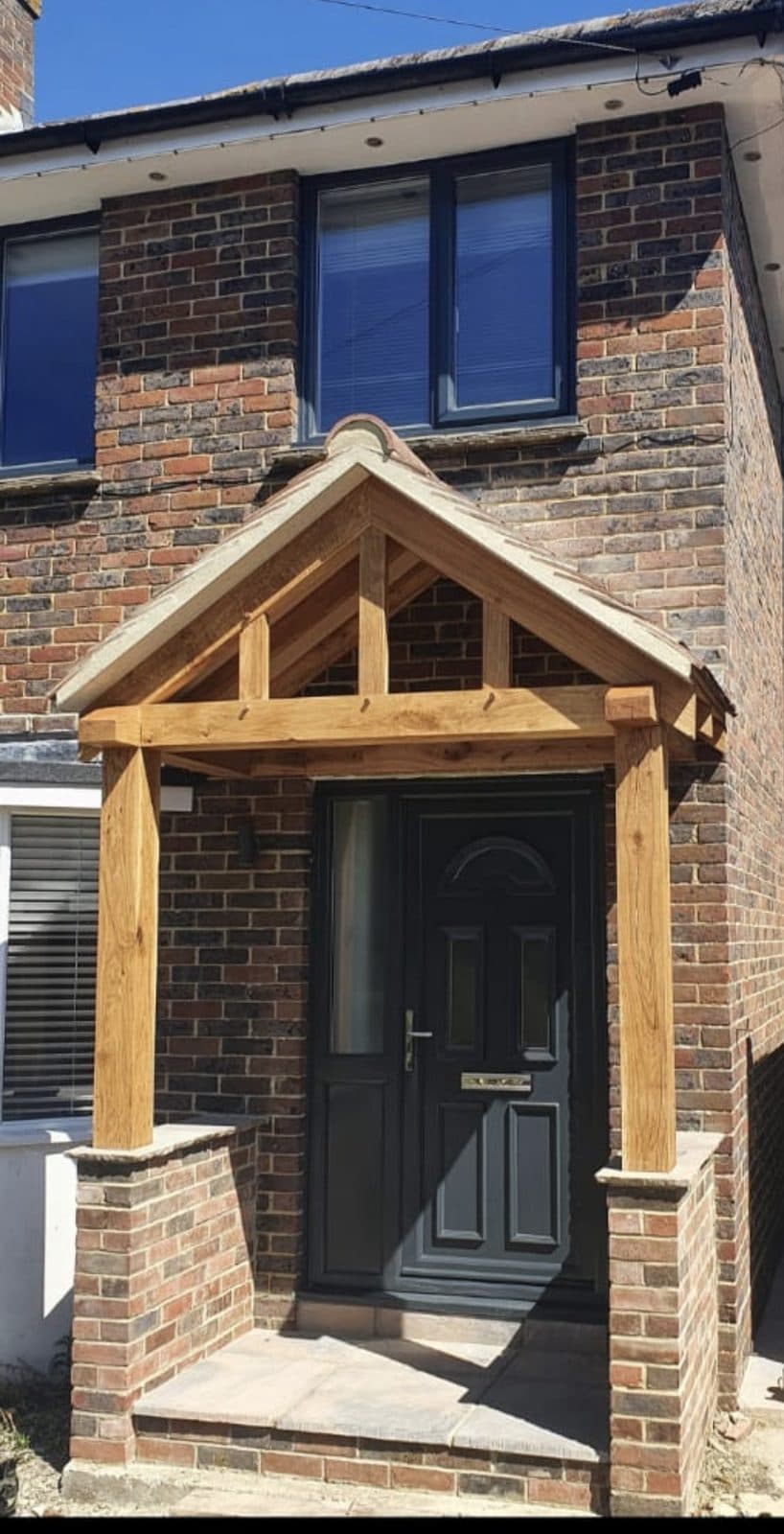 The Worcester oak porch on a brick semi — open gable and heavy posts standing on brick plinths either side of a black front door