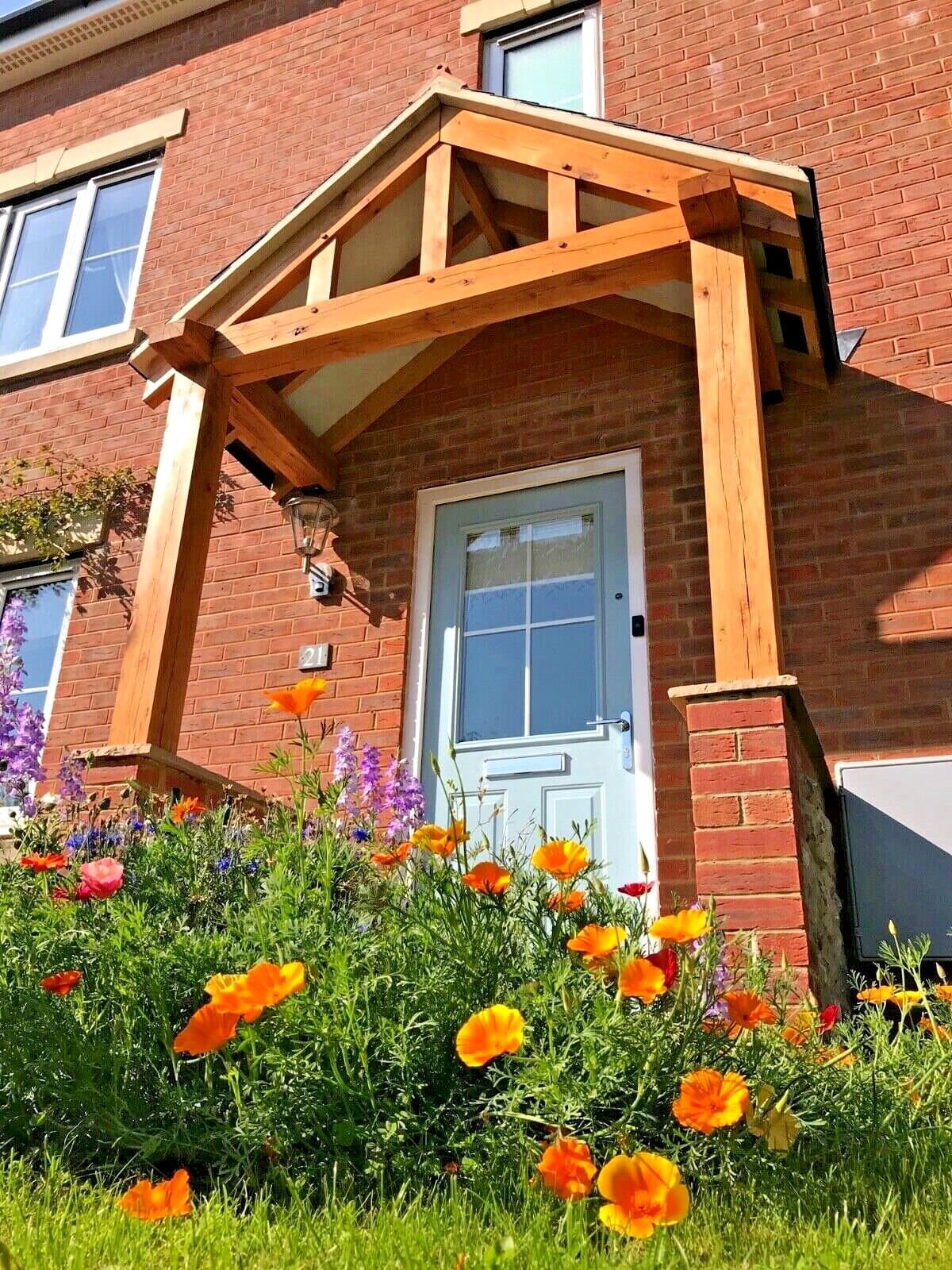The Worcester oak porch on a red-brick home — king post and struts over a pale blue front door, poppies in the border beneath