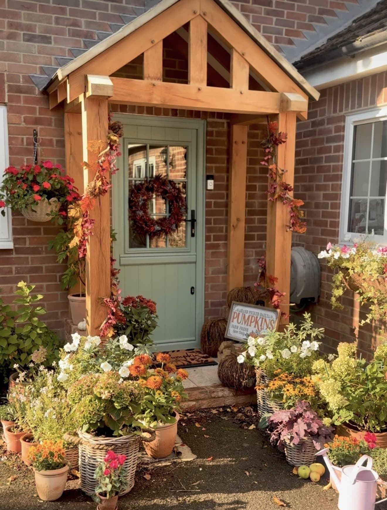 The Worcester oak porch on a red-brick country home, dressed for autumn with wreath, pumpkins and pots either side of a sage green stable door